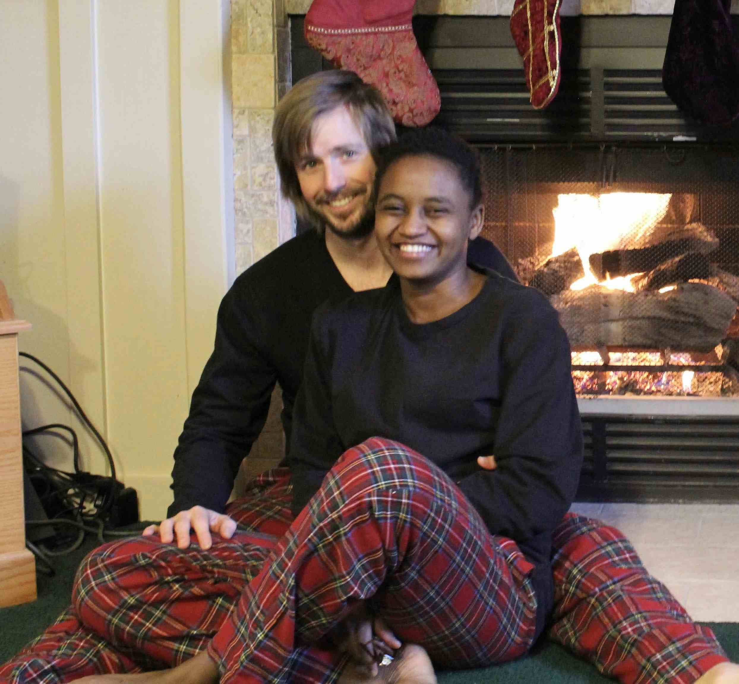 Nelly Cheboi and Tyler Cinnamon by a fireplace with festive clothes